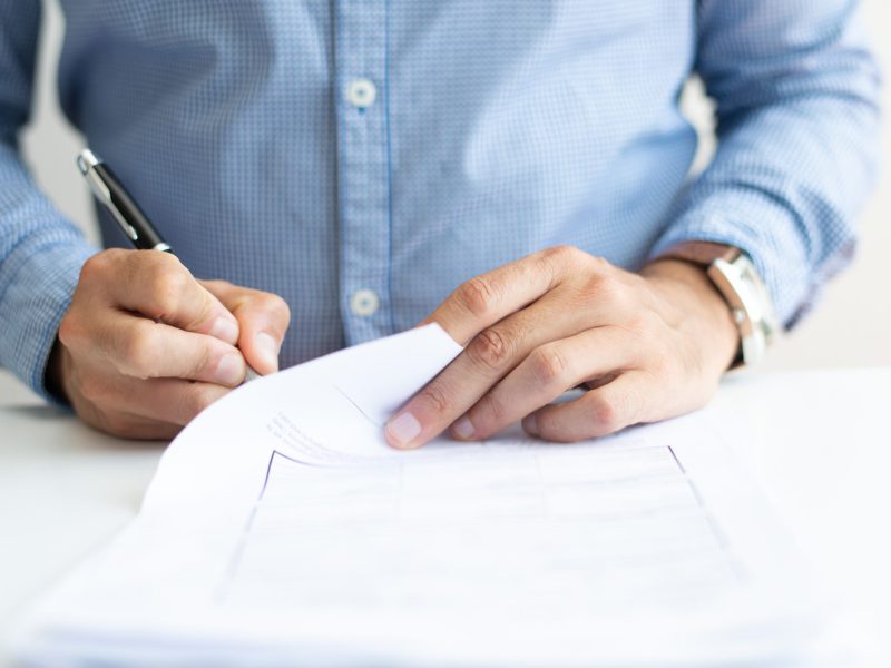 Closeup of business man signing document. Business person sitting at desk. Agreement concept. Cropped front view.